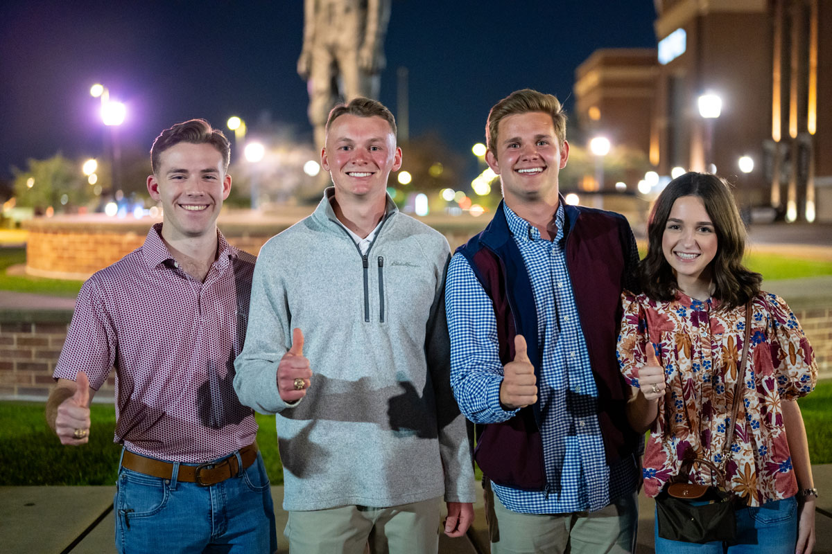 A photo of four people with the Gig'em thumbs up.