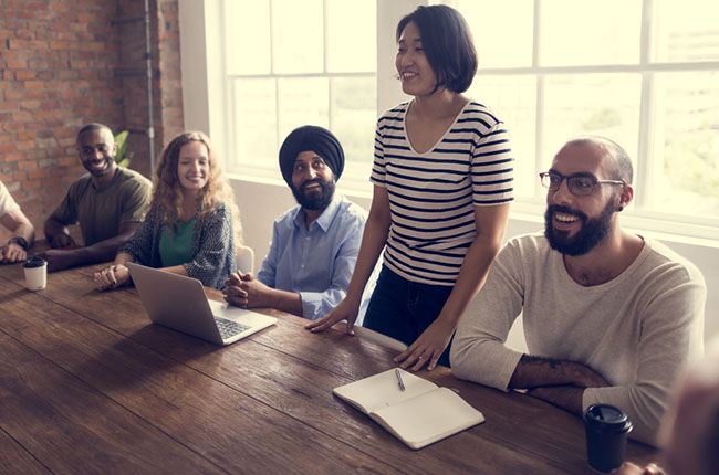 Woman stands to speak to happy group gathered around table