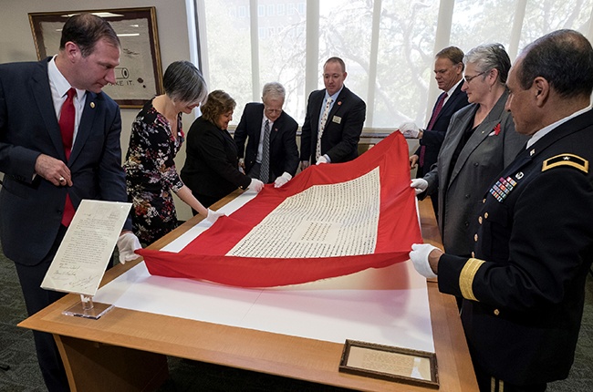 State lawmakers and Texas A&M University administrators gather around a flag honoring Aggies who served in World War I.