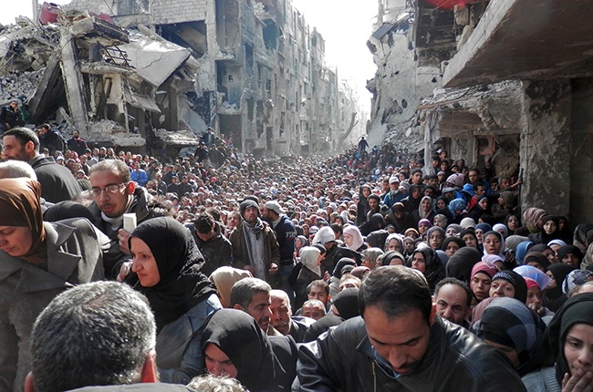 DAMASCUS, SYRIA - JANUARY 31: In this handout provided by the United Nation Relief and Works Agency (UNRWA), Residents wait in line to receive food aid distributed in the Yarmouk refugee camp on January 31, 2014 in Damascus, Syria. The United Nations renewed calls for the Syria regime and rebels to allow food and medical aid into the Palestinian camp of Yarmouk. An estimated 18,000 people are besieged inside the camp as the conflict in Syria continues. (Photo by United Nation Relief and Works Agency via Getty Images)