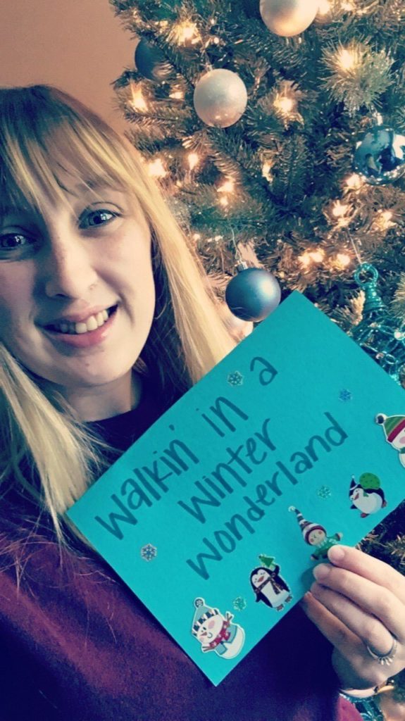 Student in front of Christmas tree with card