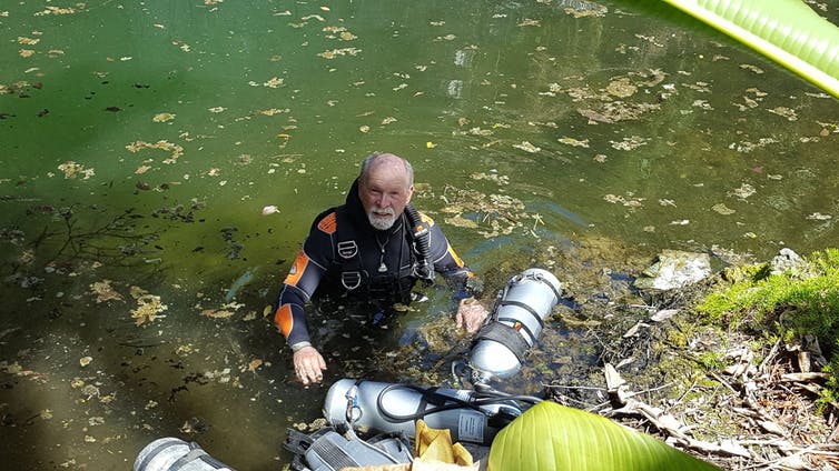 Tom Iliffe preparing for a side mount dive at Cliff Pool, Bermuda. Rather than carrying tanks on his back as in conventional scuba, a tank is clipped off under each arm, allowing him to pass through low sections in a cave where it would otherwise be impossible to go. Gil Nolan, CC BY-ND