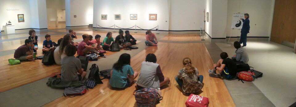 campers sit on the floor and listen to an instructor speak